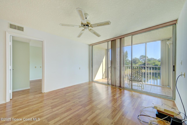 empty room featuring a water view, ceiling fan, a textured ceiling, and light wood-type flooring