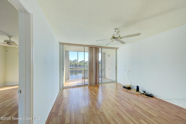 unfurnished room featuring a water view, light hardwood / wood-style flooring, a textured ceiling, ceiling fan, and a wall of windows