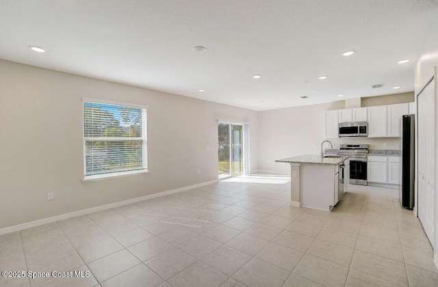 kitchen featuring sink, appliances with stainless steel finishes, light stone counters, an island with sink, and a healthy amount of sunlight