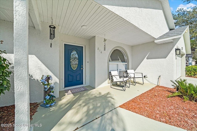 view of exterior entry featuring a shingled roof and stucco siding