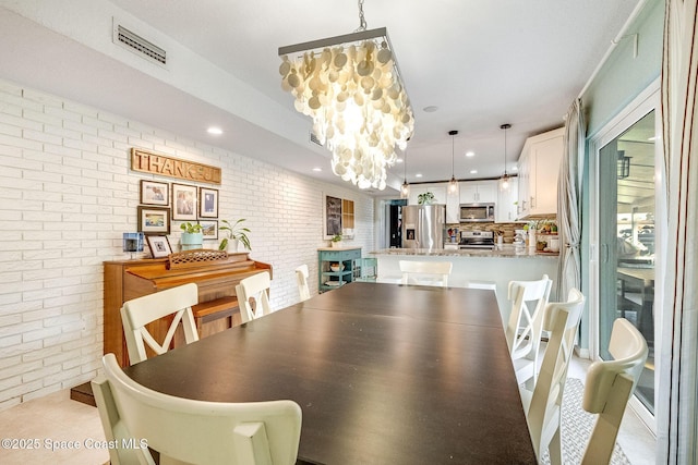 dining area with brick wall, light tile patterned floors, and a chandelier