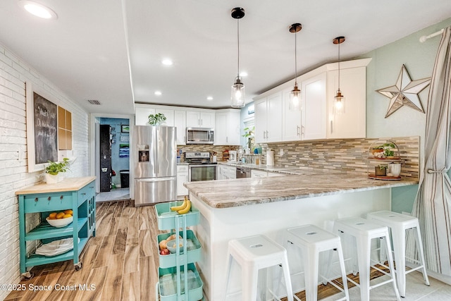 kitchen with appliances with stainless steel finishes, white cabinets, backsplash, hanging light fixtures, and kitchen peninsula