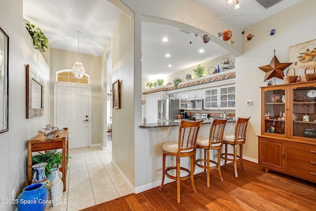 kitchen with white cabinetry, hanging light fixtures, light wood-type flooring, kitchen peninsula, and stainless steel appliances