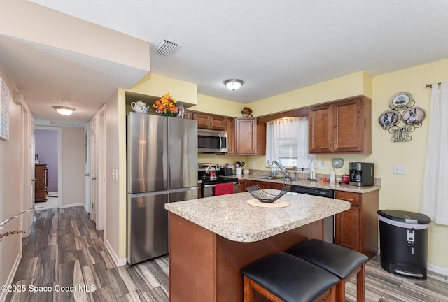 kitchen featuring sink, appliances with stainless steel finishes, a kitchen breakfast bar, wood-type flooring, and a kitchen island