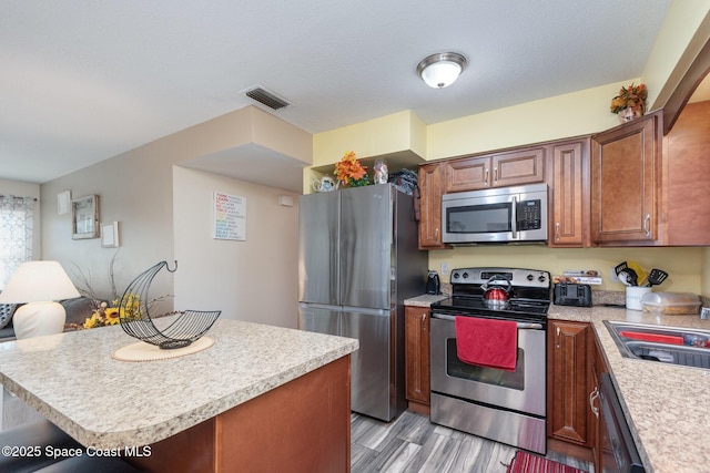 kitchen with sink, a center island, stainless steel appliances, a textured ceiling, and light hardwood / wood-style flooring