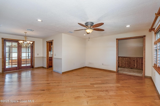 unfurnished room featuring ceiling fan with notable chandelier, a textured ceiling, and light wood-type flooring