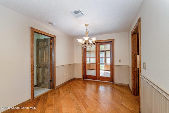 interior space with a notable chandelier, light hardwood / wood-style flooring, french doors, and a textured ceiling