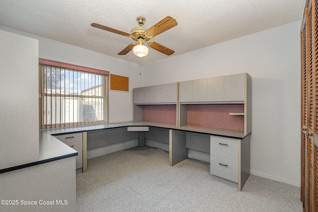 unfurnished office featuring ceiling fan, built in desk, light colored carpet, and a textured ceiling