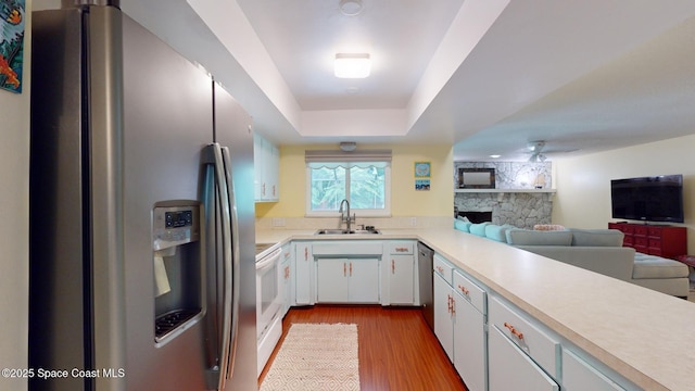 kitchen featuring sink, white cabinetry, light wood-type flooring, a raised ceiling, and stainless steel appliances