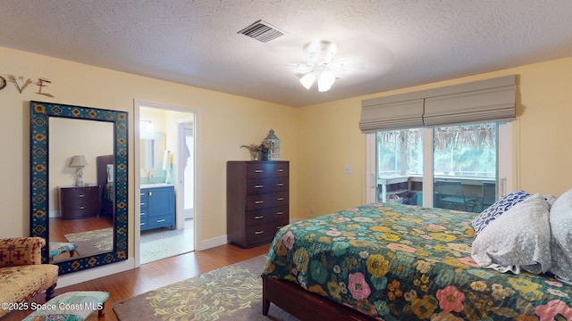 bedroom with wood-type flooring, connected bathroom, a textured ceiling, and access to outside