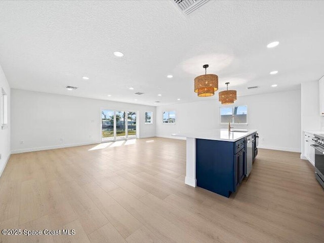 kitchen with blue cabinets, sink, hanging light fixtures, a textured ceiling, and light hardwood / wood-style floors