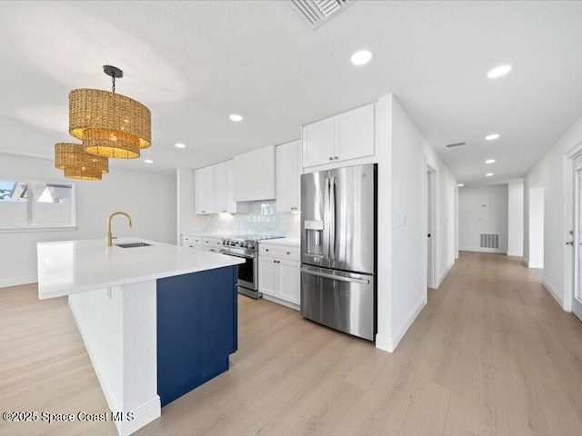 kitchen featuring appliances with stainless steel finishes, decorative light fixtures, white cabinets, a kitchen island with sink, and light hardwood / wood-style flooring