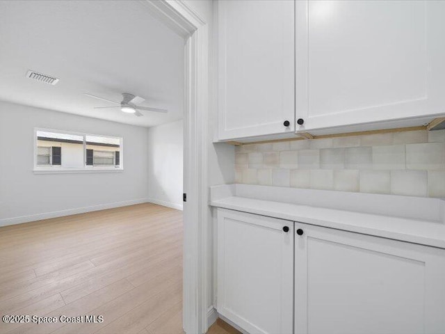 bar with tasteful backsplash, ceiling fan, white cabinets, and light wood-type flooring