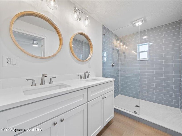 bathroom with tiled shower, vanity, and a textured ceiling