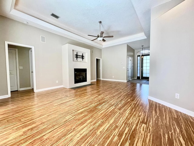 unfurnished living room featuring a tray ceiling, light hardwood / wood-style flooring, a textured ceiling, and ceiling fan