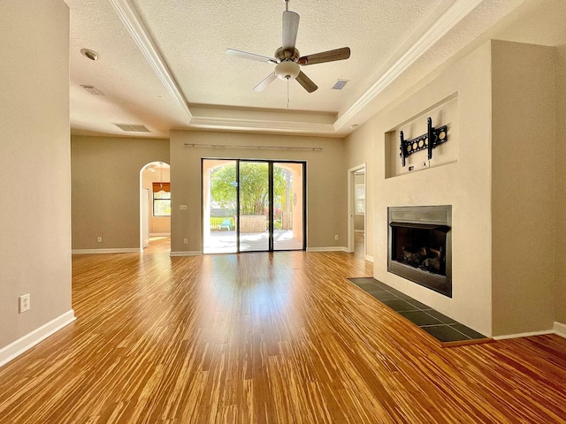 unfurnished living room with a tiled fireplace, hardwood / wood-style floors, a tray ceiling, and a textured ceiling