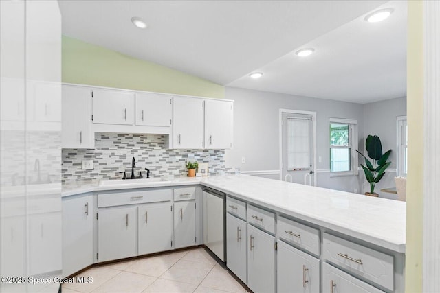 kitchen with vaulted ceiling, stainless steel dishwasher, white cabinetry, and sink