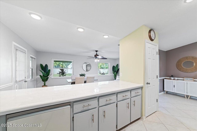 kitchen with gray cabinetry, light tile patterned floors, light stone counters, and ceiling fan