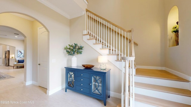 stairway featuring arched walkways, crown molding, and baseboards