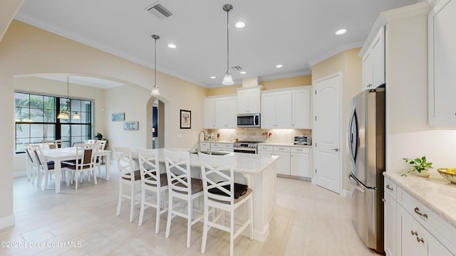 kitchen with visible vents, a sink, arched walkways, appliances with stainless steel finishes, and decorative backsplash