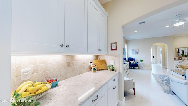 kitchen with visible vents, tasteful backsplash, white cabinetry, arched walkways, and crown molding