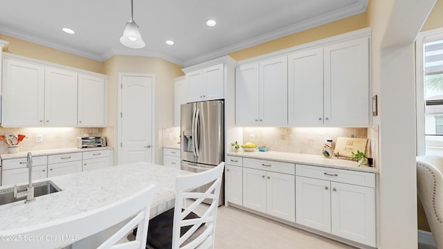 kitchen with hanging light fixtures, stainless steel fridge, white cabinetry, and a sink