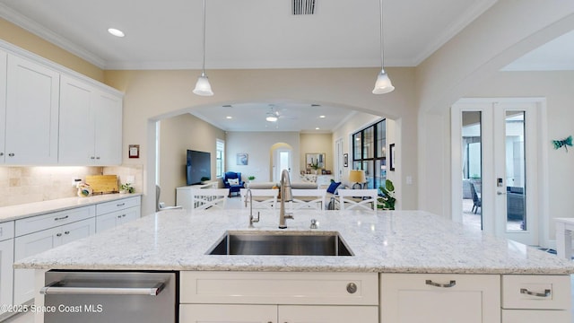 kitchen with an island with sink, a sink, open floor plan, white cabinetry, and arched walkways