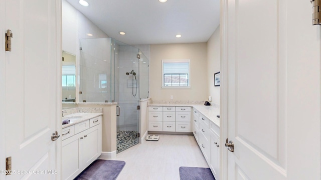 bathroom with two vanities, recessed lighting, a stall shower, wood finished floors, and a sink