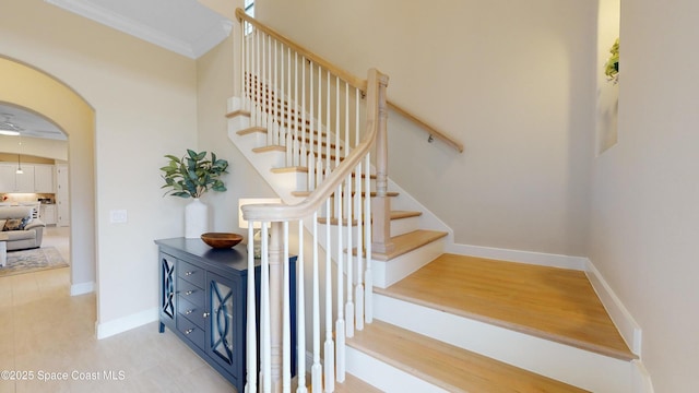 stairway with ceiling fan, baseboards, ornamental molding, wood finished floors, and arched walkways