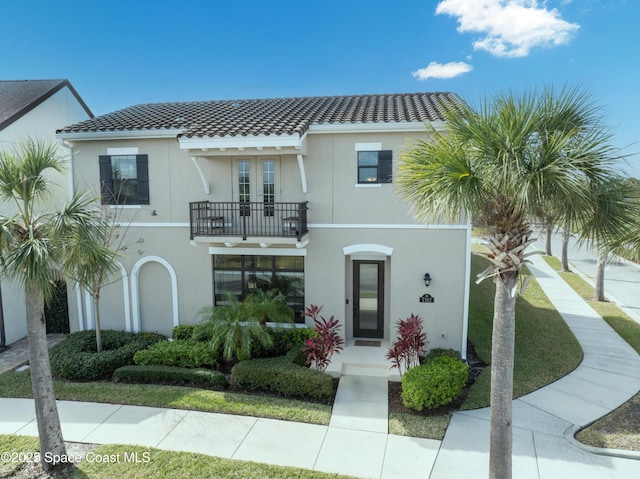 view of front of property with stucco siding, a tiled roof, french doors, and a balcony