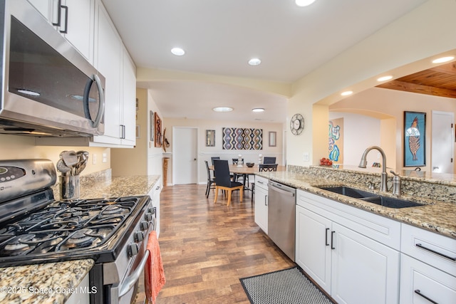 kitchen with sink, white cabinets, hardwood / wood-style flooring, stainless steel appliances, and light stone countertops