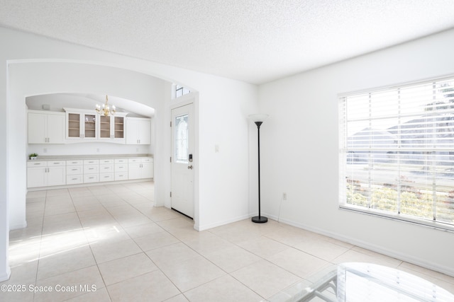 spare room featuring an inviting chandelier, light tile patterned floors, and a textured ceiling