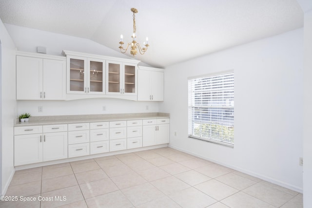 kitchen featuring a chandelier, vaulted ceiling, light tile patterned floors, pendant lighting, and white cabinets