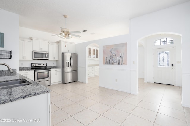 kitchen featuring sink, light tile patterned floors, appliances with stainless steel finishes, light stone counters, and white cabinets