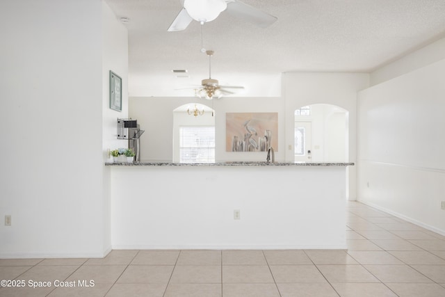 kitchen with light stone counters, kitchen peninsula, a textured ceiling, and light tile patterned floors