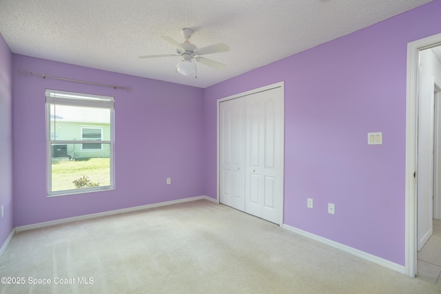 unfurnished bedroom with a textured ceiling, light colored carpet, a closet, and ceiling fan