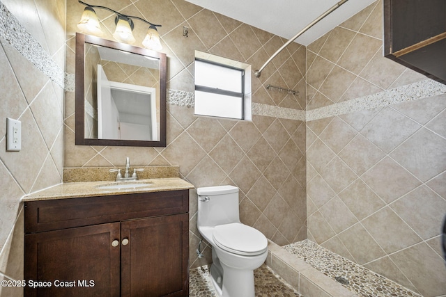 bathroom with tile walls, vanity, toilet, and a tile shower