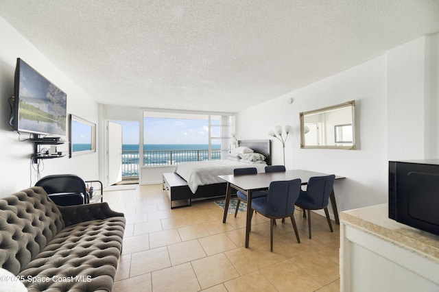 bedroom with a water view, access to exterior, a textured ceiling, and light tile patterned floors