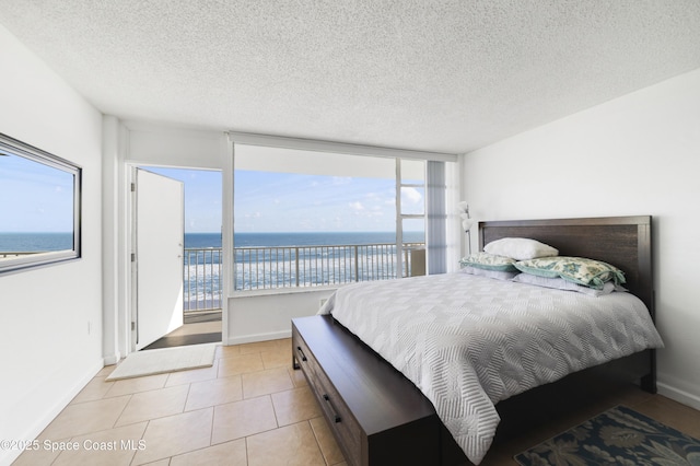 bedroom featuring access to outside, light tile patterned flooring, a textured ceiling, and a water view