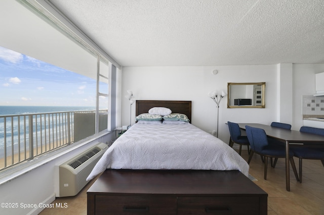 tiled bedroom with a water view, an AC wall unit, a textured ceiling, and a view of the beach