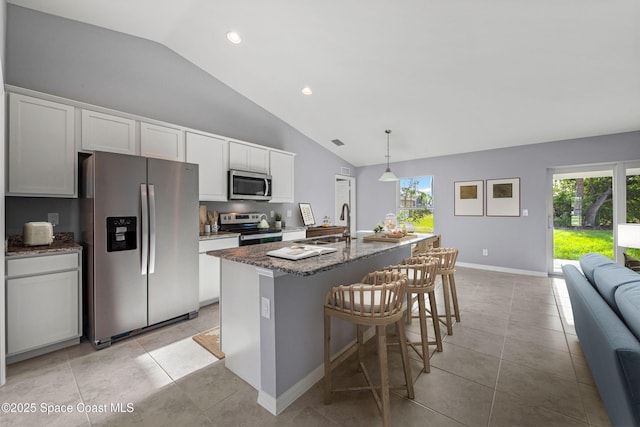 kitchen with pendant lighting, lofted ceiling, white cabinets, stainless steel appliances, and a center island with sink