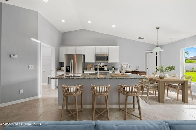 kitchen featuring vaulted ceiling, pendant lighting, dark stone countertops, white cabinets, and stainless steel appliances