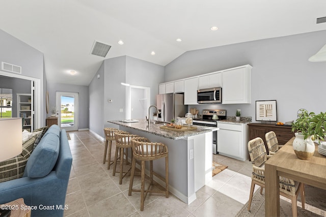 kitchen featuring lofted ceiling, light tile patterned floors, a kitchen island with sink, stainless steel appliances, and light stone countertops