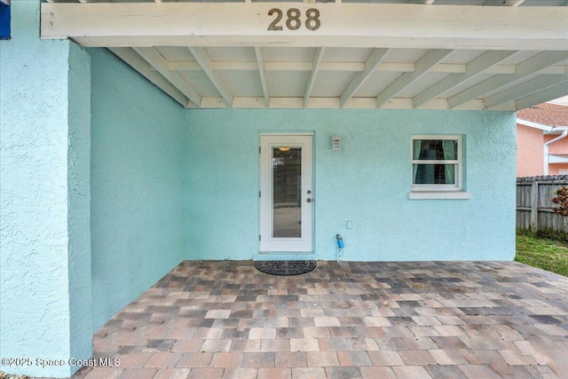 doorway to property featuring fence and stucco siding