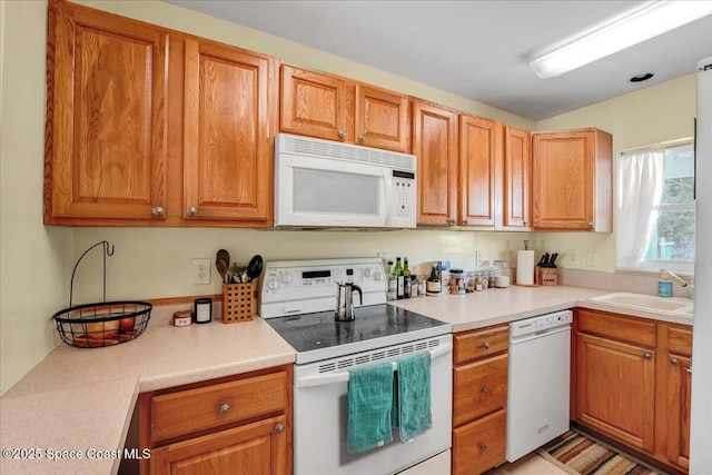 kitchen with brown cabinetry, white appliances, light countertops, and a sink