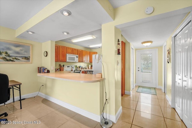 kitchen with white microwave, light tile patterned flooring, range with electric stovetop, light countertops, and brown cabinets