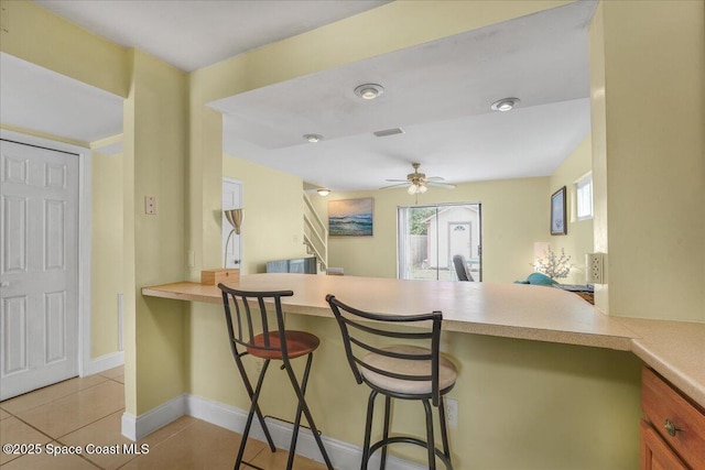 kitchen with light countertops, a breakfast bar area, light tile patterned flooring, and a peninsula