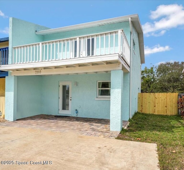 view of front of property featuring a patio, fence, a balcony, and stucco siding