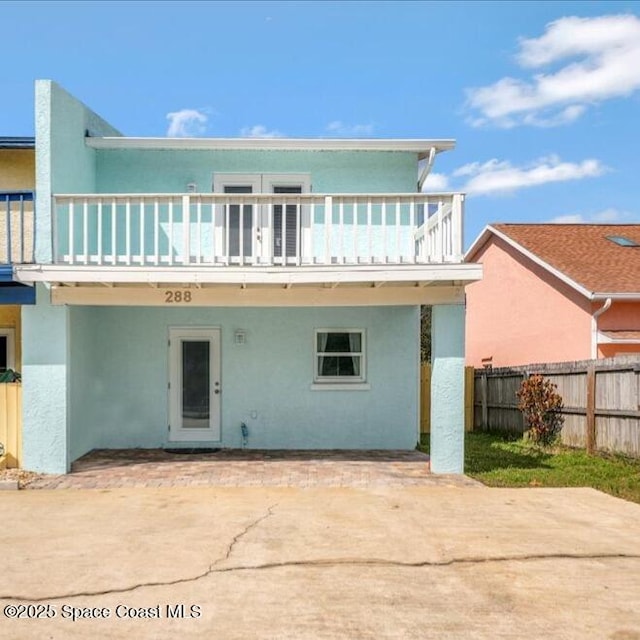 back of house featuring driveway, fence, a balcony, and stucco siding