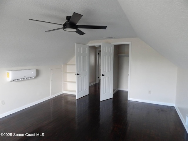 bonus room featuring lofted ceiling, dark hardwood / wood-style flooring, ceiling fan, a textured ceiling, and a wall unit AC